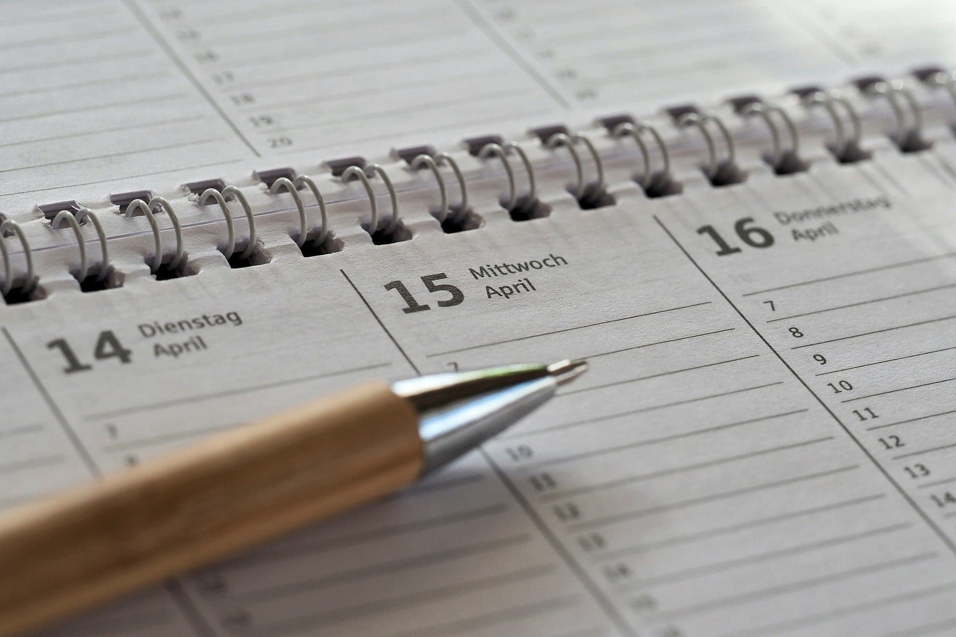 A spiral desk planner open to a blank week with a pen resting on the page