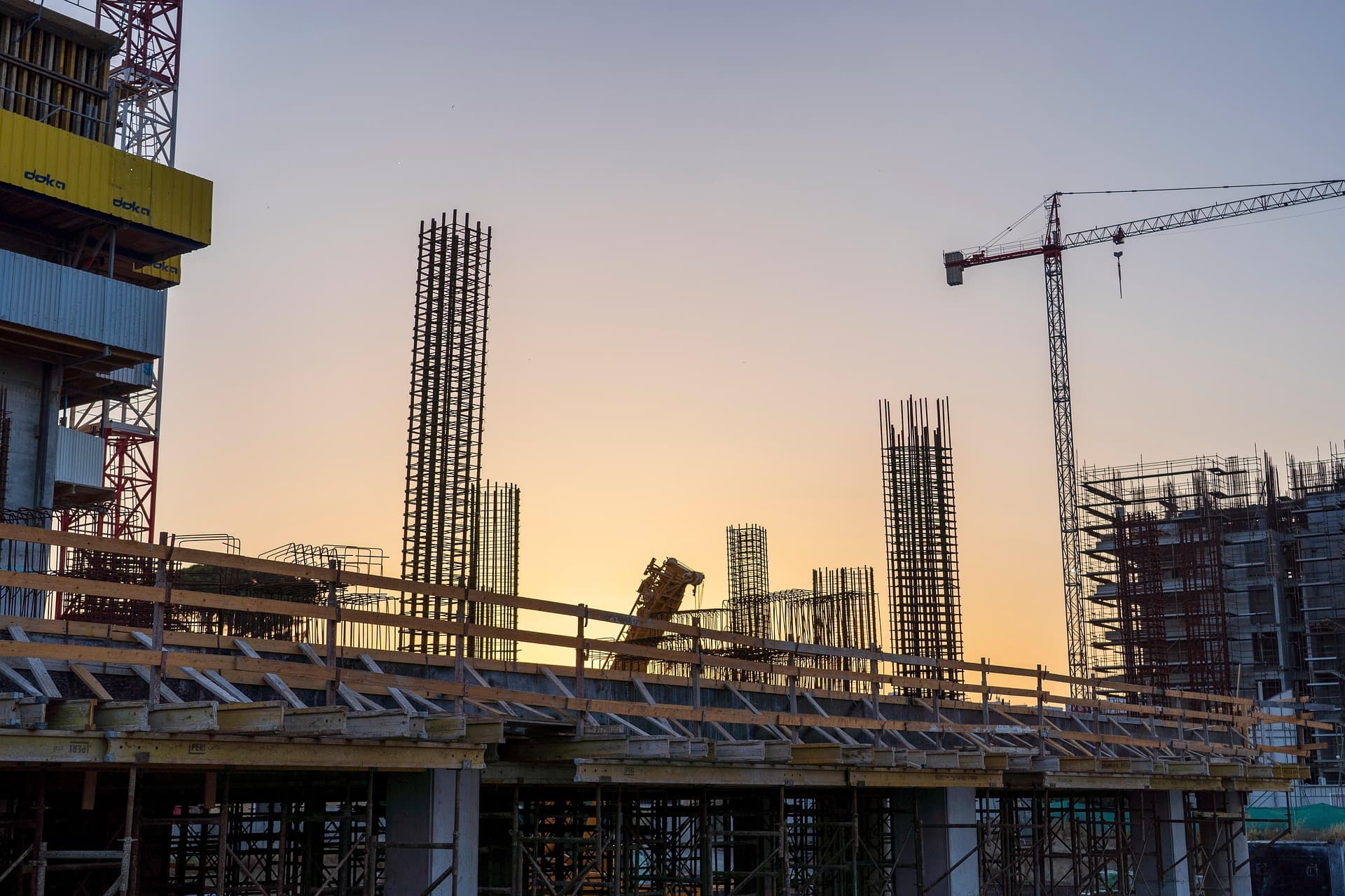 Construction site with rebar columns and a tower crane at dusk