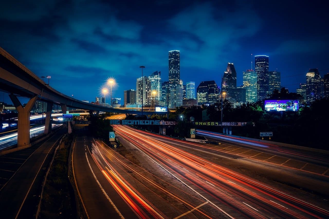 City skyline at night above a freeway streaked with traffic light trails