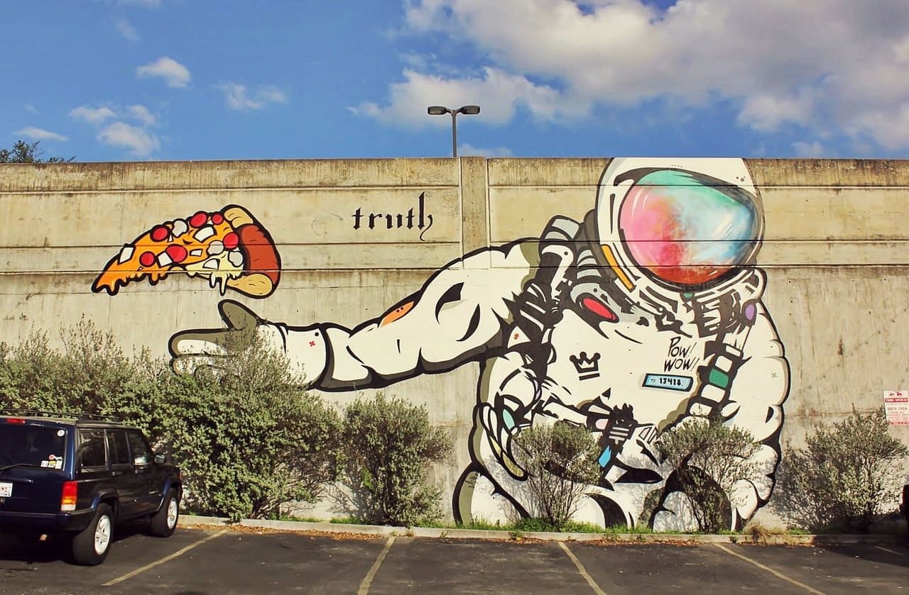 Street mural of an astronaut reaching toward a slice of pizza beside the word truth